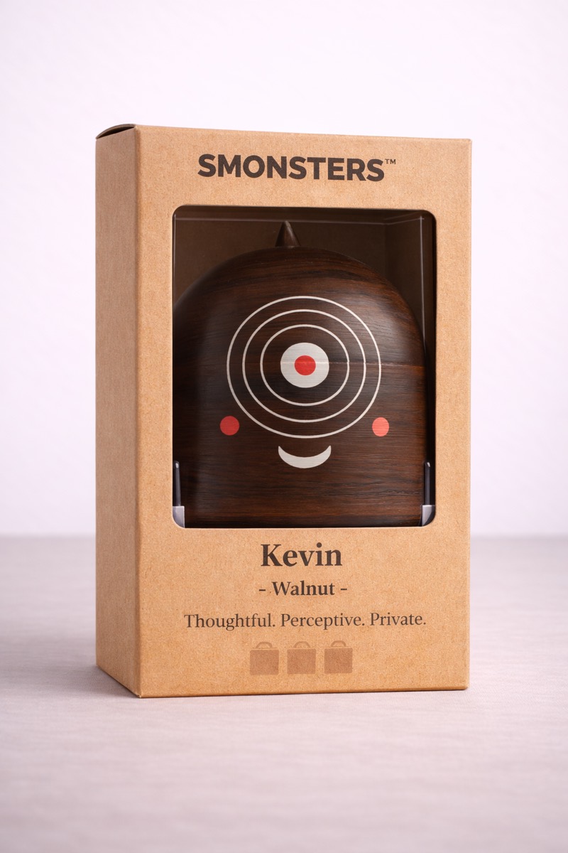 Kevin, a dark walnut figurine with a target-shaped eye and a small red centre, in a kraft box with a window cut into the front.